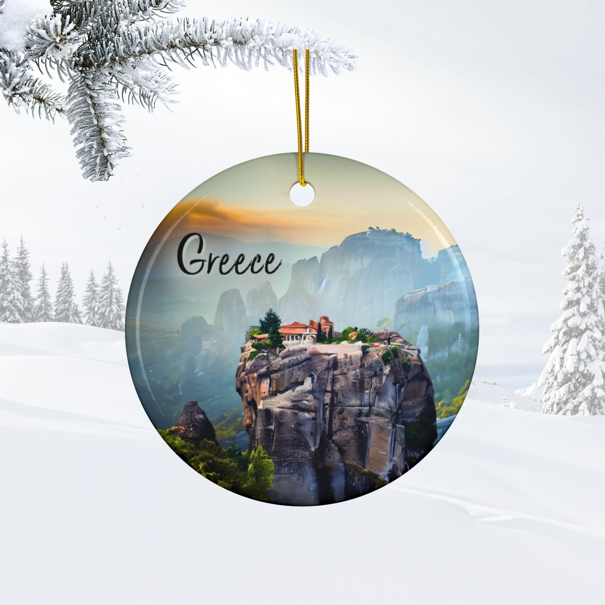 A round double-sided ornament with “Greece” written on it, featuring a scenic view of Meteora’s cliffside monasteries. The Meteora Greece ornament hangs from a gold string against a snowy outdoor background with pine branches.